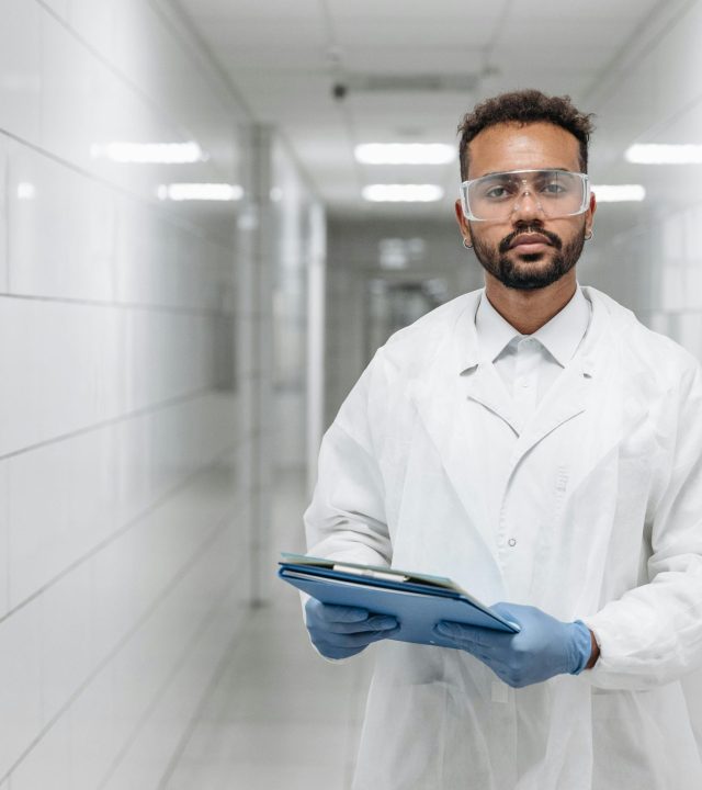 pexels-photo-8442620-8442620 Portrait of a scientist in a laboratory hallway wearing protective goggles and gloves.